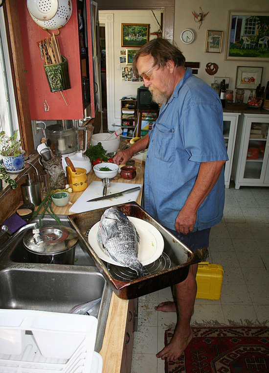 Pops works his magic in his characteristically cluttered home kitchen. Note the bare feet-Pops was occasionally spotted walking around town without shoes, and he sometimes came into the On The Water office barefoot. We never really knew whether he had forgotten his shoes or simply didn’t care, but we suspect it was the latter.