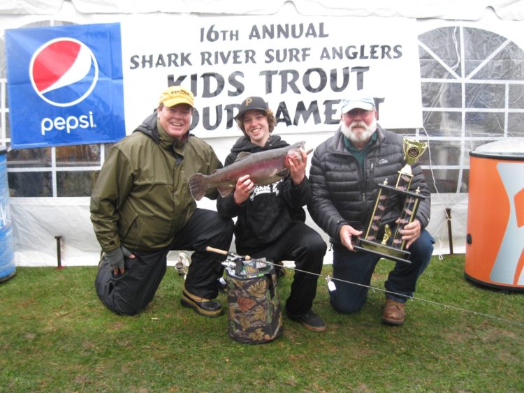 Jack Byscek with the 7-pound, 9-ounce-rainbow trout that won the annual Shark River Surf Anglers Trout Contest for Kids Greg Hueth SRSA president left and club vice president Ken Morse.
